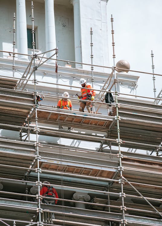 free-photo-of-construction-workers-standing-on-the-scaffolding-outside-of-a-building-in-city